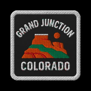 Może przedstawiać: Haftowana naszywka z napisem "GRAND JUNCTION COLORADO" w kolorze białym, nad krajobrazem. Scena przedstawia pomarańczowe formacje skalne, zieloną rzekę i żółte słońce na czarnym tle, obramowane białą obwódką.