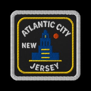 May include: Embroidered patch featuring the words "Atlantic City New Jersey" in white, arched over a blue building and a small orange circle. The patch has a black background, a yellow border, and a white stitched edge.
