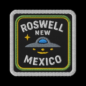 Op de afbeelding: Geborduurde patch met de tekst "ROSWELL NEW MEXICO" in het wit, een grijze UFO en een gele ster. De patch heeft een zwarte achtergrond met groene en gele randen en een witte gestikte rand.