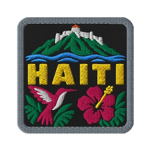 May include: A square embroidered patch with a gray border on a black background. It features a white fortress atop a green mountain, a blue river, the yellow text HAITI, a pink hummingbird, and a large pink hibiscus flower with green leaves.