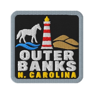 Puede incluir: Un parche bordado cuadrado con fondo negro y borde gris. Presenta un caballo blanco, un faro de rayas rojas y blancas, olas azules y dunas de arena beige. El texto dice OUTER BANKS N. CAROLINA en letras blancas y amarillas.