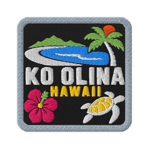 Puede incluir: Un parche bordado cuadrado con fondo negro que muestra una montaña verde, una laguna azul, una palmera, una flor de hibisco rosa y una tortuga marina blanca. El texto dice KO OLINA en blanco y HAWAII en amarillo con un borde gris claro.