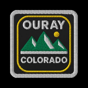 May include: Embroidered patch featuring the text "OURAY COLORADO" above and below a mountain range graphic. The patch has a black background with a yellow border and white stitching. The mountains are green and white, and a yellow sun is visible.