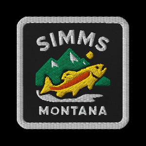 May include: Embroidered patch featuring the word "SIMMS" above a mountain range and a leaping fish. The fish is yellow with orange accents, and the mountains are green. The word "MONTANA" is below the fish, all on a black background.