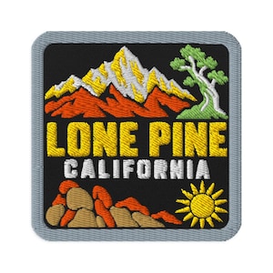 May include: A square embroidered patch with a black background featuring a mountain range in yellow and orange, a green tree, and a yellow sun. The text LONE PINE is embroidered in yellow, and CALIFORNIA is in white, all bordered by a gray edge.