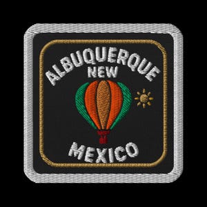 May include: Embroidered patch featuring a hot air balloon in orange, green, and brown, with the text "ALBUQUERQUE NEW MEXICO" in white. The patch has a black background, a gold border, and a white stitched edge. A small yellow sun is also present.