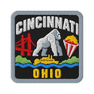 Puede incluir: Un parche bordado cuadrado con fondo negro y borde gris. Presenta el texto blanco CINCINNATI en la parte superior y OHIO en amarillo en la parte inferior. El diseño incluye un gorila blanco, un puente rojo, un barco amarillo y palomitas.