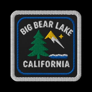 May include: Embroidered patch featuring the text "BIG BEAR LAKE CALIFORNIA". The patch has a black background with a green tree, a yellow mountain, and a white mountain with a star. The patch is bordered with white and blue stitching.