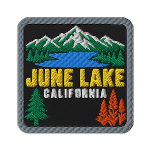 Pode incluir: Um emblema bordado quadrado com fundo preto apresentando uma cordilheira com picos nevados sobre um lago azul. O texto JUNE LAKE está em amarelo, com CALIFORNIA em branco abaixo. Um pinheiro verde e plantas laranja estão na parte inferior.