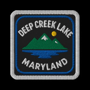 May include: Embroidered patch with the text "Deep Creek Lake Maryland." The patch has a black background, blue border, and white stitched edge. The design includes green mountains, a blue lake, and a yellow sun.
