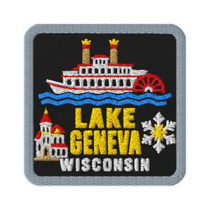 May include: A square embroidered patch with a black background and a gray border. It features a white and red paddlewheel boat on blue water, a small white building with a red roof, a white snowflake, and the yellow text LAKE GENEVA and WISCONSIN.