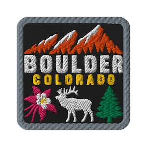 May include: A square embroidered patch with a black background and a gray border. It features orange mountain peaks, the white text BOULDER, yellow text COLORADO, a pink columbine flower, a white elk silhouette, and a green pine tree.