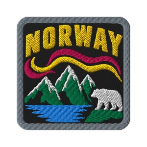 Puede incluir: Un parche bordado cuadrado con fondo negro que presenta el texto amarillo NORWAY en la parte superior. Debajo del texto hay auroras boreales estilizadas en rosa y amarillo, montañas verdes con cumbres nevadas blancas, un lago azul y un oso polar blanco.