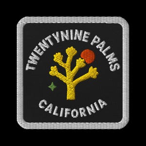 Puede incluir: Parche bordado con el texto "TWENTYNINE PALMS CALIFORNIA" en blanco, arqueado arriba y abajo de un árbol de Josué amarillo y un sol rojo. Una estrella verde está a la izquierda. El parche tiene un borde blanco y un fondo negro.
