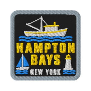 Puede incluir: Un parche bordado cuadrado con fondo negro y borde gris. Presenta un barco blanco y amarillo sobre olas azules, un velero azul, un faro blanco y el texto amarillo HAMPTON BAYS junto al texto blanco NEW YORK.