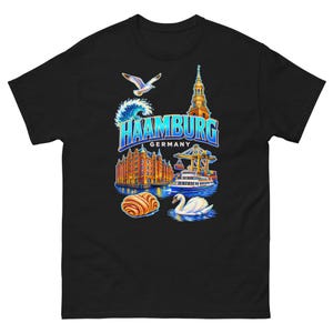 Peut inclure: Un t-shirt noir à manches courtes avec une impression graphique colorée du texte HAAMBURG GERMANY, une mouette, une vague, une flèche d'église, un bâtiment en briques, une grue portuaire, un ferry, une pâtisserie et un cygne blanc sur l'eau.