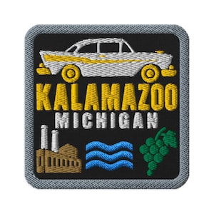 May include: A square embroidered patch with a black background and a grey border. It features a white vintage car with yellow accents, the yellow text KALAMAZOO, white text MICHIGAN, a brown factory building, blue waves, and a green grape cluster.
