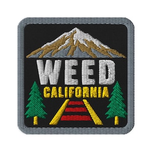 May include: A square embroidered patch with a gray border on a black background. It features a snow-capped mountain above the white text WEED and yellow text CALIFORNIA. Two green pine trees flank a central graphic of red and yellow railroad tracks.