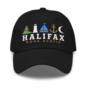 Può includere: Un cappellino da baseball nero con una grafica raffigurante un pino verde, un faro bianco, una barca a vela blu, un'ancora marrone e una luna crescente bianca. Sotto le icone, il testo riporta HALIFAX in bianco e NOVA SCOTIA in marrone.