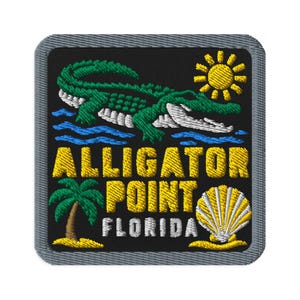 Könnte beinhalten: Ein quadratischer gestickter Aufnäher mit grauem Rand auf schwarzem Hintergrund. Er zeigt einen grünen Alligator, eine gelbe Sonne, blaues Wasser, eine grüne Palme und eine weiß-gelbe Muschel. Der Text lautet ALLIGATOR POINT FLORIDA in Gelb.