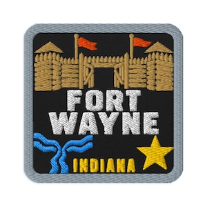 Puede incluir: Un parche bordado cuadrado con borde gris sobre fondo negro. Presenta un fuerte de madera color canela con dos banderas naranjas, el texto blanco FORT WAYNE, un gráfico de río azul, el texto amarillo INDIANA y una estrella amarilla.
