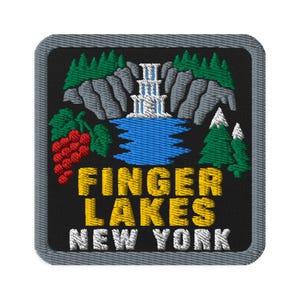 May include: A square embroidered patch with a black background featuring a waterfall, grey cliffs, green pine trees, and red grapes. The text FINGER LAKES is in yellow, and NEW YORK is in white. The patch has a grey border with a stitched edge.