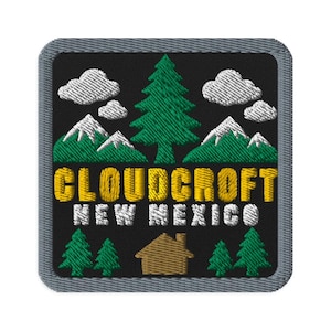 Puede incluir: Un parche bordado cuadrado con fondo negro y borde gris. Presenta un pino verde, nubes blancas y montañas verdes con picos blancos. El texto CLOUDCROFT en amarillo y NEW MEXICO en blanco se sitúa sobre una cabaña de color marrón.