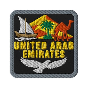 Puede incluir: Un parche bordado cuadrado con borde gris sobre fondo negro. Presenta un barco dhow blanco, una montaña amarilla, una palmera verde y un camello naranja. El texto UNITED ARAB EMIRATES está en amarillo, con un pájaro blanco debajo.