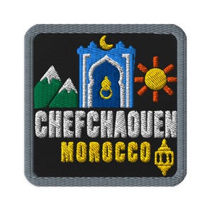 May include: A square embroidered patch with a black background and a grey border. It features green mountains, a blue arched doorway with a yellow crescent moon and door knocker, a yellow sun, and the text CHEFCHAOUEN MOROCCO in white and yellow.