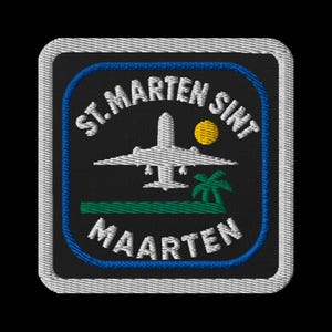 Peut inclure: Écusson brodé avec le texte "ST. MARTEN SINT MAARTEN" en blanc, avec un bord bleu. Le motif comprend un avion blanc, un soleil jaune et un palmier vert. L'écusson a un fond noir et une bordure blanche.