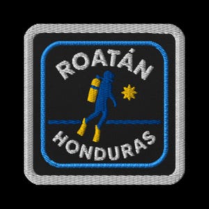 Könnte beinhalten: Gestickter Aufnäher mit dem Text "ROATAN HONDURAS" in Weiß, einer blauen Taucher-Silhouette und einer gelben Sonne. Der Aufnäher hat einen schwarzen Hintergrund mit blauen und weißen Rändern.