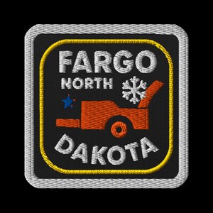 Puede incluir: Parche bordado con las palabras "FARGO NORTH DAKOTA" en blanco, un copo de nieve y una quitanieves naranja sobre un fondo negro. El parche tiene un borde amarillo y un borde cosido gris.
