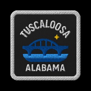 May include: Embroidered patch featuring the city name "Tuscaloosa" above a blue bridge illustration and the word "Alabama" below. The patch has a black background with a white border and a small yellow star.