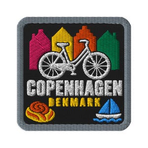 May include: A square embroidered patch with a black background and a grey border. It features a white bicycle silhouette, colourful house outlines, a yellow cinnamon roll, a blue sailboat, and the white text COPENHAGEN DENMARK.