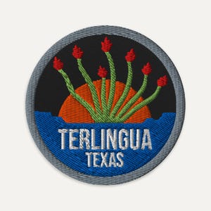 May include: A circular embroidered patch with a gray border. The design features a black background with an orange sun, green ocotillo plants, and a blue base. The white text reads TERLINGUA TEXAS in a bold, sans-serif font.