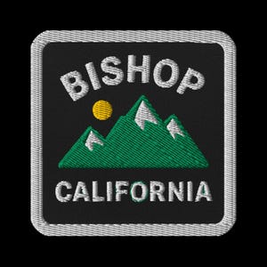 May include: Embroidered patch featuring the text "BISHOP CALIFORNIA" above a green mountain range with white snow caps and a yellow sun. The patch has a black background and a white border.