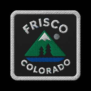 May include: Embroidered patch featuring the text "FRISCO COLORADO" in white, arched above and below a green mountain scene with two trees and a blue lake. The patch has a black background and a white stitched border.