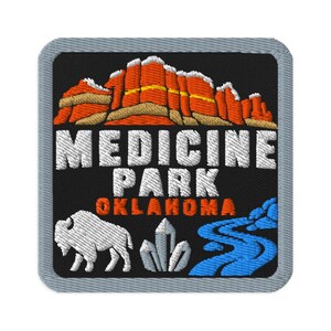 May include: A square embroidered patch with a gray border on a black background. It features orange and tan rock formations, white text reading MEDICINE PARK, orange text reading OKLAHOMA, a white bison, white crystals, and a blue winding river.