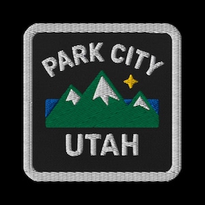 May include: Embroidered patch featuring the text "PARK CITY UTAH" in white, arched above a green mountain range with white snow caps and a yellow star. The patch has a black background and a white border.