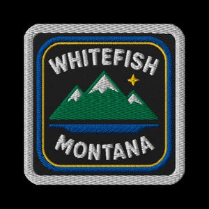 Puede incluir: Parche bordado con el texto "WHITEFISH MONTANA" en blanco, sobre una cordillera verde con picos nevados. Una estrella amarilla está encima de las montañas y un lago azul debajo. El parche tiene un fondo negro con bordes azules y amarillos.