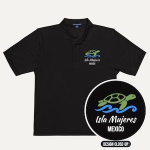 May include: A black short-sleeved polo shirt featuring a small embroidered graphic on the left chest of a green sea turtle swimming above blue waves, with the text Isla Mujeres MEXICO printed below the turtle in white lettering.