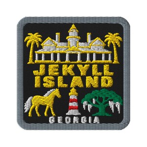Pode incluir: Um emblema bordado quadrado com fundo preto e borda cinza. Apresenta um edifício amarelo, palmeiras, o texto amarelo JEKYLL ISLAND, um cavalo amarelo, um farol vermelho e branco, uma árvore verde e o texto branco GEORGIA.