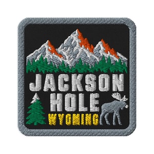 Può includere: Una toppa ricamata quadrata con sfondo nero che raffigura una catena montuosa con cime bianche e arancioni sopra una foresta verde. Il testo JACKSON HOLE è in bianco, WYOMING in giallo, con un pino verde e un alce grigio.