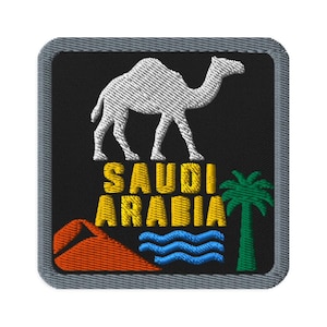 Puede incluir: Un parche bordado cuadrado con borde gris sobre fondo negro. Presenta un camello blanco, el texto amarillo SAUDI ARABIA, una duna triangular roja, líneas onduladas azules que representan agua y una palmera verde en un diseño estilizado.