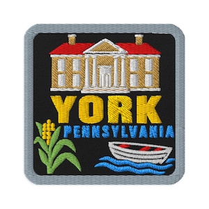 May include: A square embroidered patch with a black background and a grey border. It features a tan building with a red roof, the yellow text YORK, the blue text PENNSYLVANIA, a green corn stalk, and a white boat on blue water waves.