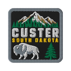 May include: A square embroidered patch with a black background and a gray border. It features a white and brown mountain range above green pine trees. The text CUSTER is in white, SOUTH DAKOTA is in yellow, with a white bison and a green pine tree.