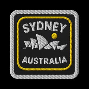 Op de afbeelding: Geborduurde patch met het woord "SYDNEY" boven een gestileerde afbeelding van het Sydney Opera House en het woord "AUSTRALIA". De patch heeft een zwarte achtergrond met witte, gele en grijze details.