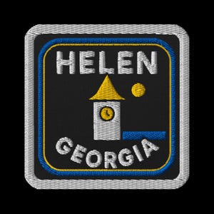 May include: Embroidered patch featuring the text "HELEN GEORGIA" in white, arched over a white tower with a yellow roof and clock face. A yellow dot is to the right of the tower. The patch has a black background with blue and yellow borders.