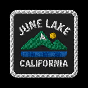 Può includere: Toppa ricamata con la scritta "JUNE LAKE CALIFORNIA" in bianco, arcuata sopra una scena di montagna e lago. Le montagne sono verdi, il sole è giallo e il lago è blu, su sfondo nero con bordo bianco.
