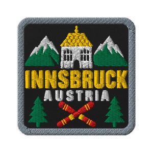 Könnte beinhalten: Ein quadratischer Stickaufnäher mit schwarzem Hintergrund und grauem Rand. Er zeigt ein weißes Gebäude mit gelbem Dach, flankiert von zwei grünen Bergen mit weißen Spitzen. Darunter steht der Text INNSBRUCK AUSTRIA über zwei gekreuzten roten Skiern.